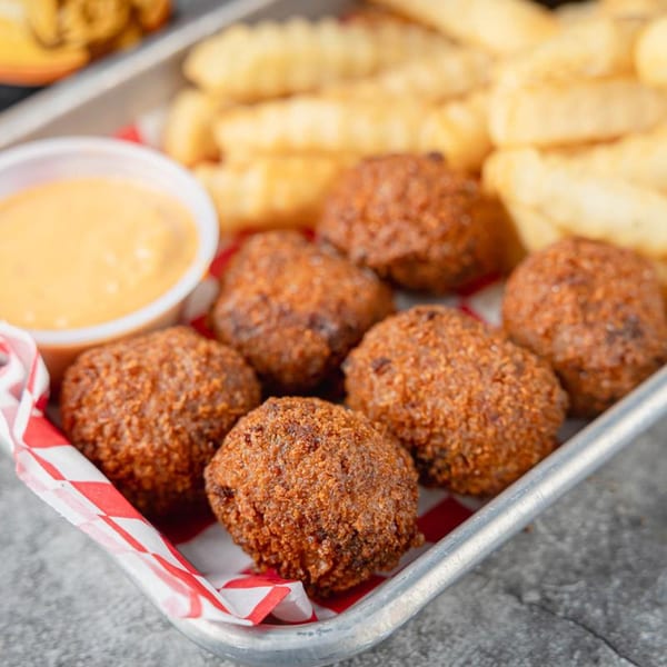 A tray of crispy hush puppies, crinkle-cut fries, and a side of dipping sauce.