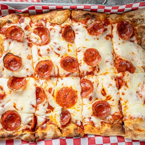 Close-up of a rectangular pepperoni pizza, cut into squares, on a red and white checkered liner.
