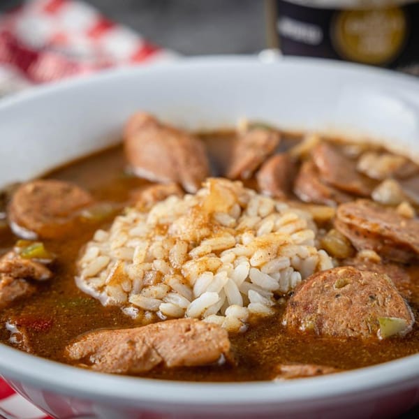 Close-up of a bowl of Cajun gumbo with sausage, chicken, and a scoop of rice.