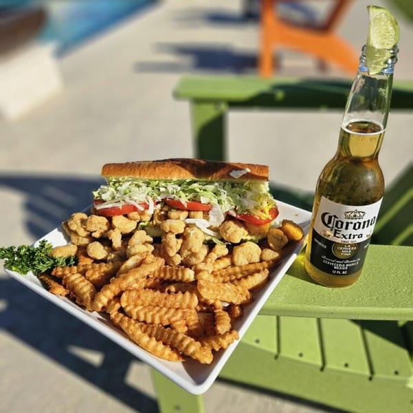 A fried shrimp po'boy with fries and a Corona beer with lime on a green outdoor chair.