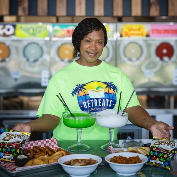 A smiling woman in a Retreats t-shirt presents daiquiris, fried food, and Cajun dishes.