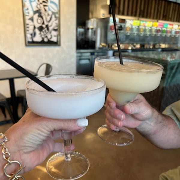 Two people clinking glasses of frozen daiquiris at Retreats New Orleans Style Daiquiris & Eats.