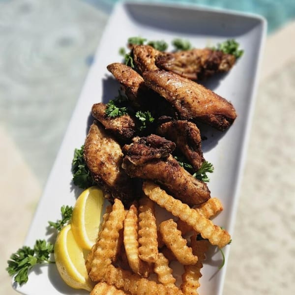Crispy Cajun chicken wings and crinkle-cut fries with lemon wedges and parsley on a white platter.