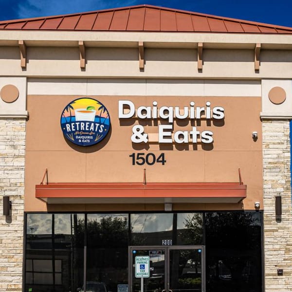 Exterior of Retreats New Orleans Style Daiquiris & Eats, featuring its logo, name, and address.
