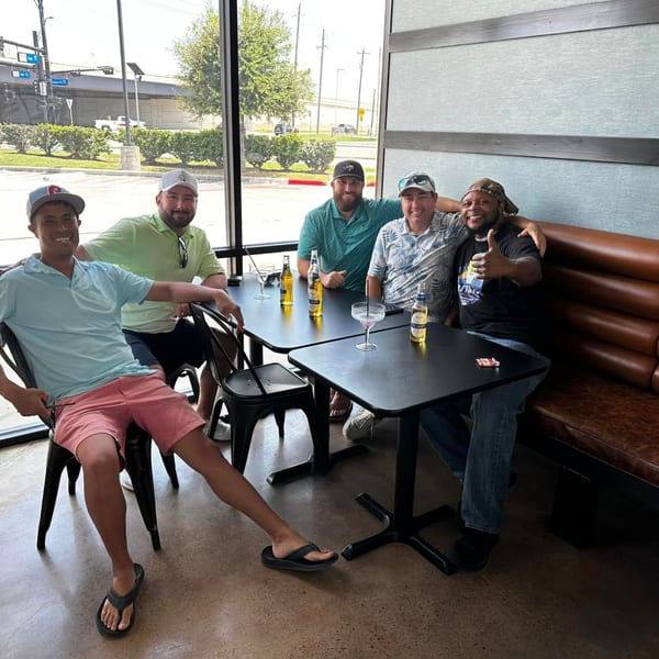 Five men smiling and relaxing at tables with drinks inside Retreats New Orleans Style Daiquiris & Eats.